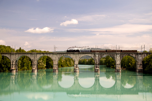 Old steam train on the Lucinico bridge near Gorizia, Italy, Europe. Lots of black and gray steam hiding the locomotive, full frame.