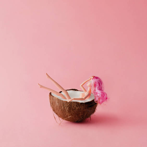 Doll with pink hair bathing in coconut. Summer concept.