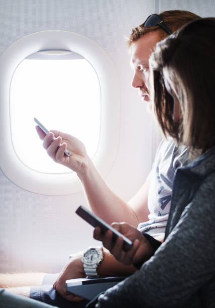 istock Man holding a smartphone while seated by an airplane window 812088306