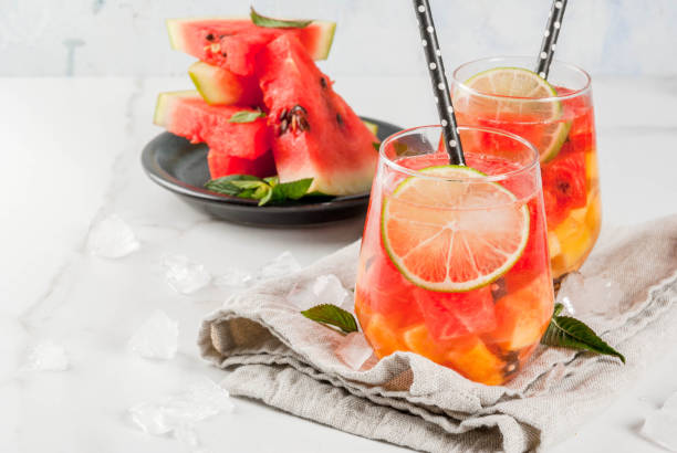 Watermelon summer sangria Summer drinks and cocktails. Lemonade, homemade sangria with fresh watermelon, lime, mint and pineapple. In two glasses,  on a white marble table. Copy space sangria stock pictures, royalty-free photos & images