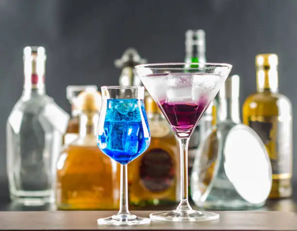 Photo of Colorful drink on the background of bottles in original shapes, cocktail drink with ice cubes