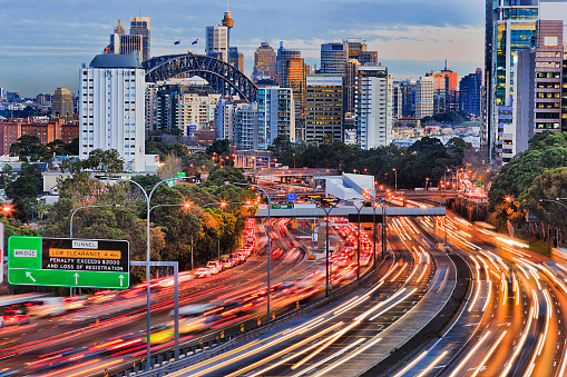 Long exposure blurred vehicle motion on multi-lane Warringah freeway going through North Sydney in Sydney, Australia. Headlights and backlights during rush hour commute towards Sydney harbour bridge and CBD towers.