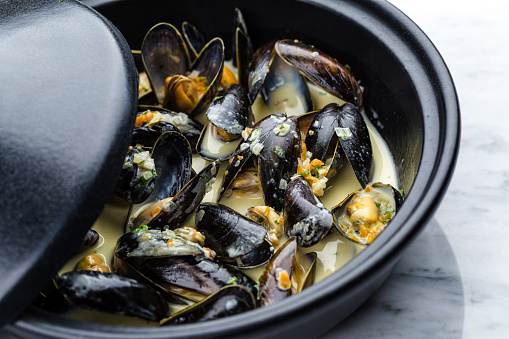 Soup of mussels creamy in black bowl on marbel surface.