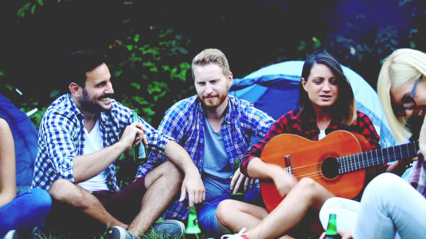 istock Four friends sitting next to campfire and singing song 812217678