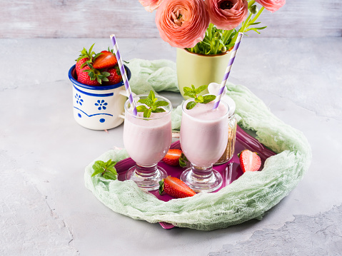 Strawberry milk shake in glasses for romantic summer healthy breakfast. Summer table setting with ranunculus flowers