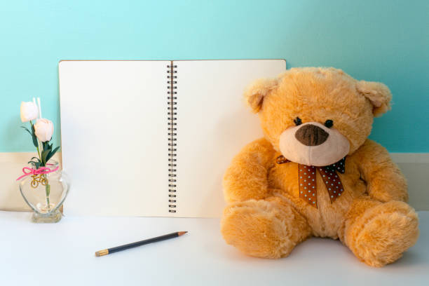 istock Teddy bear with pink flower and blank page notebook with pencil on blue pastel background, warm look with warm window light 812370848