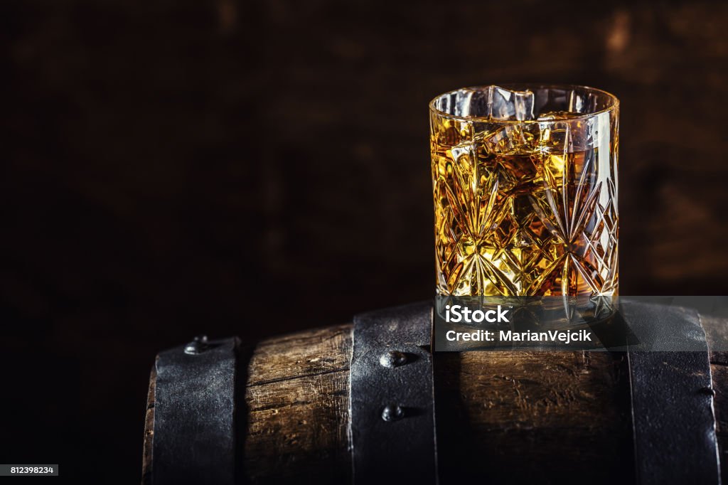 Whiskey drink. Glass of whiskey on old wooden barrel Whiskey drink. Glass of whiskey on old wooden barrel. Bourbon Whiskey Stock Photo