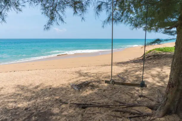 Photo of Swing with tree blue sky and clouds background, blue sea and white sand beach on Mai Khao beach at Phuket Thailand is most popular for tourist. Copy space for vacation.