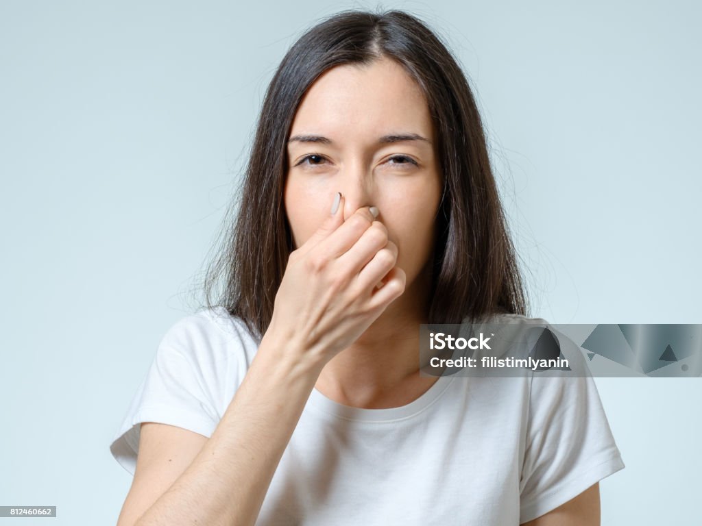 Girl covers nose with hand showing that something stinks isolated on gray background Unpleasant Smell Stock Photo