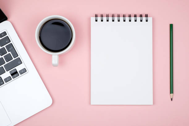 Modern pink office desk table with laptop and blank notebook page for input the text. Top view, flat lay