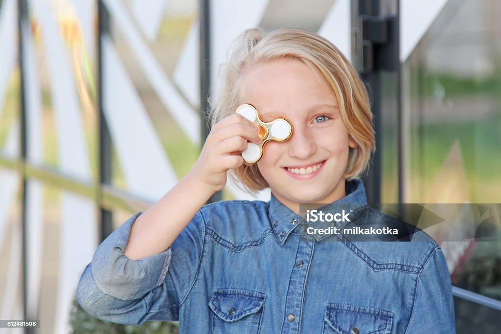 Cheerful cute school aged girl playing with a gold fidget spinner. A popular trendy toy. Beautiful cheerful school girl playing with a gold fidget spinner. A popular trendy toy for the development of fine motor skills in children and adults. Arts Culture and Entertainment Stock Photo