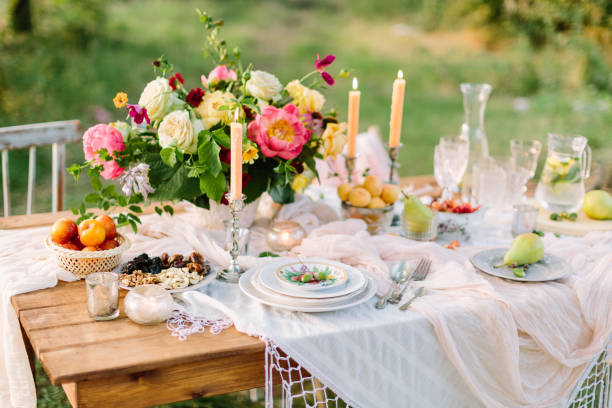 women's day, wedding, celebration, romance, picnic, nature concept - gorgeous table setting with snow white tablecloth, dishes, clear wine-glasses, silver candleholders and various fruits stock photo