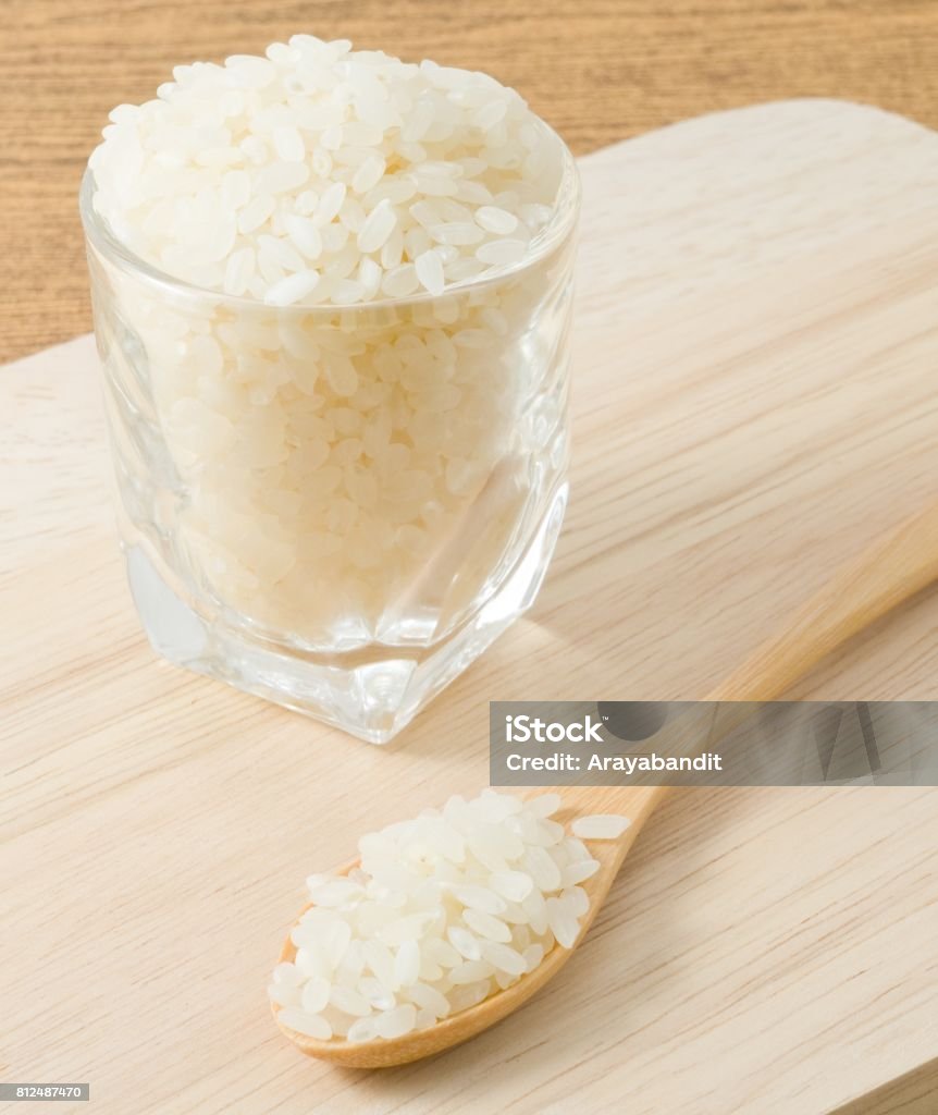 Japanese Rice in A Wooden Spoon and Glass Cup Japanese Cuisine, Raw and Uncooked Japanese Rice in A Wooden Spoon and A Glass Cup on Wooden Board. Basmati Rice Stock Photo