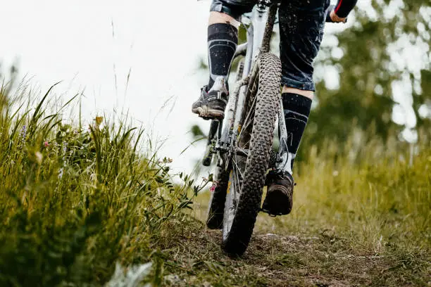 Photo of closeup mud mountain bike wheel and legs of cyclist