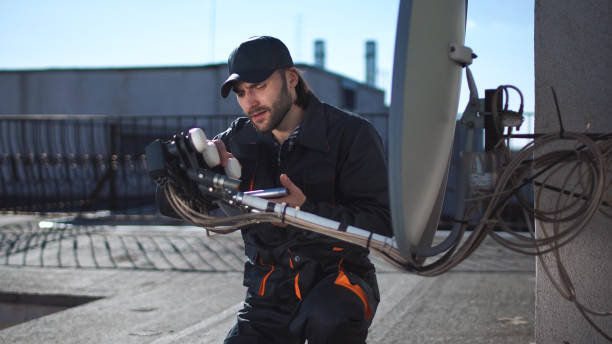 Engineer or technician checking an antennae with touchpad Engineer or technician checking or installing a parabolic dish television antennae and booster on the roof of an urban high-rise using digital tablet installing tv stock pictures, royalty-free photos & images