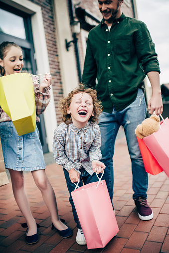 excited children holding shopping bags while happy father looking on them