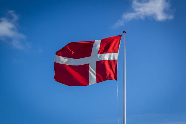 istock Danish flag in sunshine against blue sky with clouds, horizontal 812609108