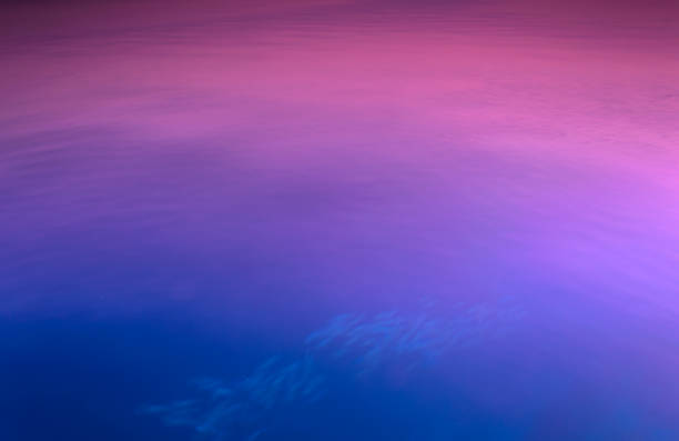 Long exposure with very interesting light reflection on the surface of the indian ocean with purple and blue tones at the sunset, somewhere on the Maldives and some fishes swimming in the ocean with motion blur.
