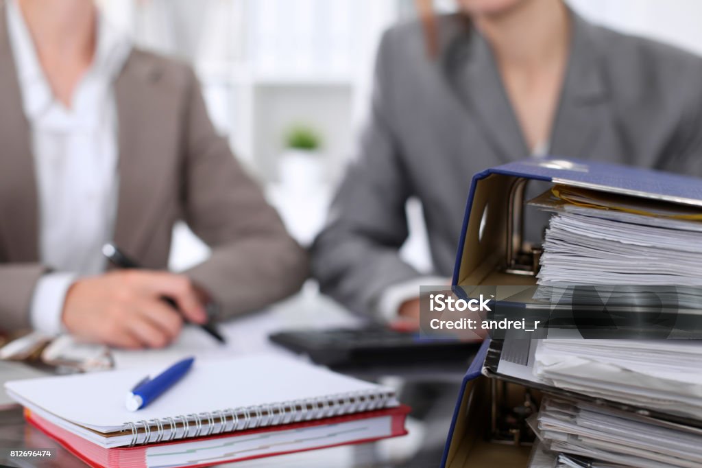 Binders with papers are waiting to be processed with businessman and secretary back in blur. Internal Revenue Service inspector checking financial document. Binders with papers are waiting to be processed with businessman and secretary back in blur. Internal Revenue Service inspector checking financial document Document Stock Photo