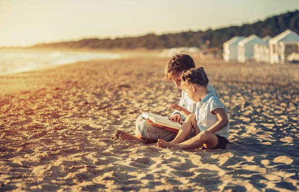 Children reading a book on beach at sunset