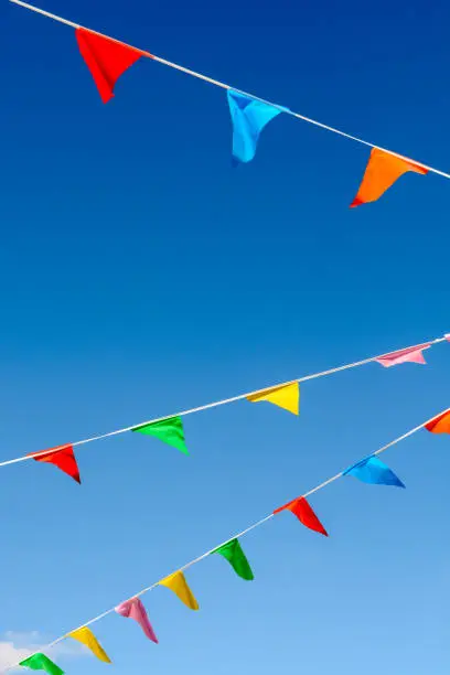 Garlands of colorful party flags blowing in the wind against blue sky.