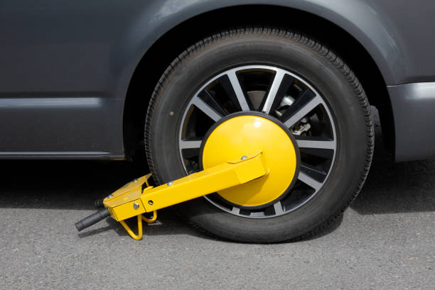 Wheel clamp attached Harnosand, Sweden - July 5, 2017: One clamped car wheel with a yellow wheel clamp. car boot stock pictures, royalty-free photos & images