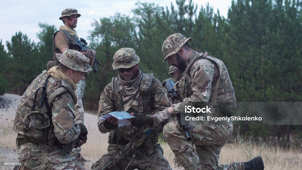 Military people navigating on battlefield Two soldiers sitting in nature and using map and gps tracker for navigation. Mercenary - Human Role Stock Photo
