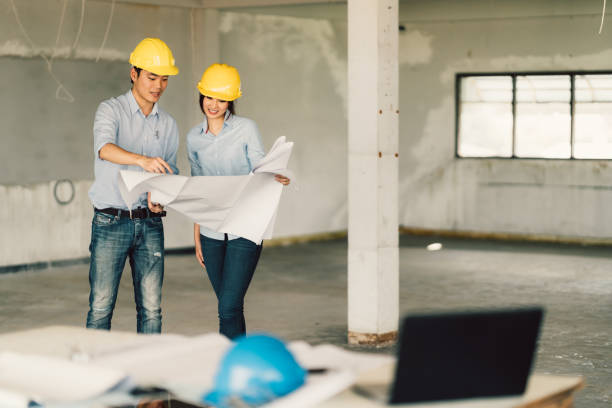 istock Young Asian engineers couple working on building blueprint at construction site. Civil engineering, industrial, or home renovation concept. With copy space 812773676