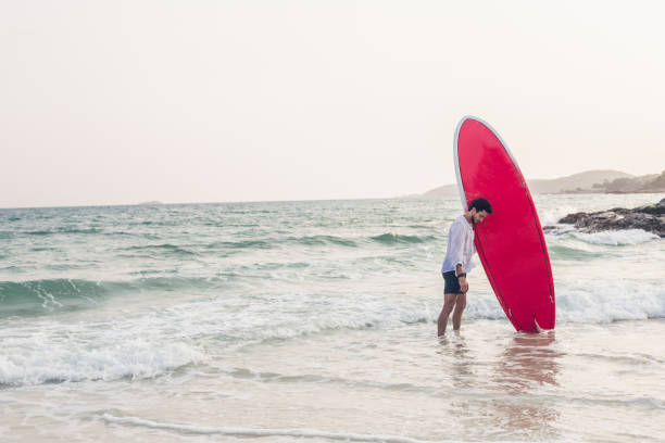 istock Young man with surfboard in the water 812782436