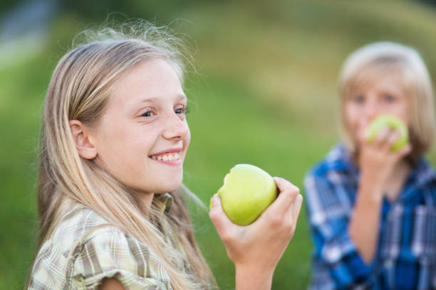 młoda dziewczyna jedząca jabłko na pikniku rodzinnym - apple eating little girls green zdjęcia i obrazy z banku zdjęć