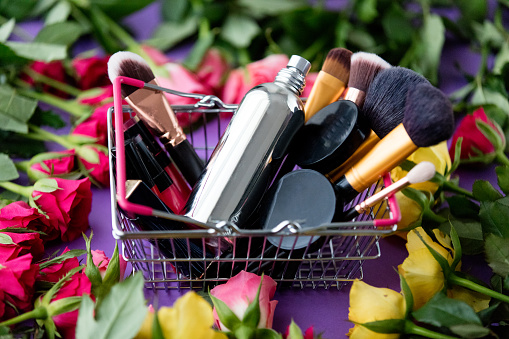 beautiful yellow and pink rose flowers and shopping basket with cosmetics close-up on purple background