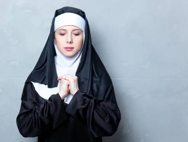 Young serious nun on grey background