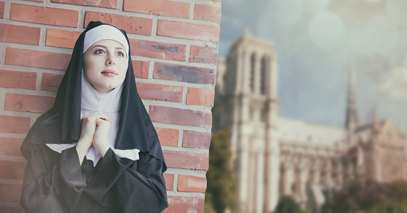 Young smiling nun standing near brick wall and Notre-Dame de Paris on background
