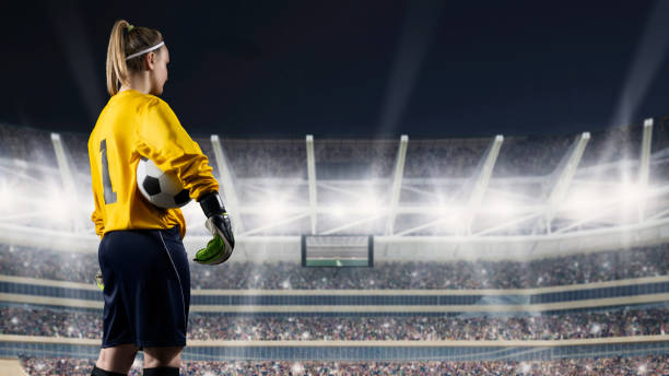 female goalkeeper standing with the ball against the crowded stadium at night female football player in yellow uniform holding ball on full stadium on background football league stock pictures, royalty-free photos & images