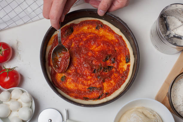 istock Closeup hand of chef adding tomato sauce on the pizza dough 812881598
