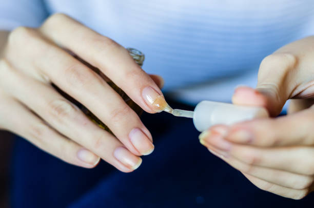 Woman with long fingers and nails applying transparent nail base at home, close up photo stock photo