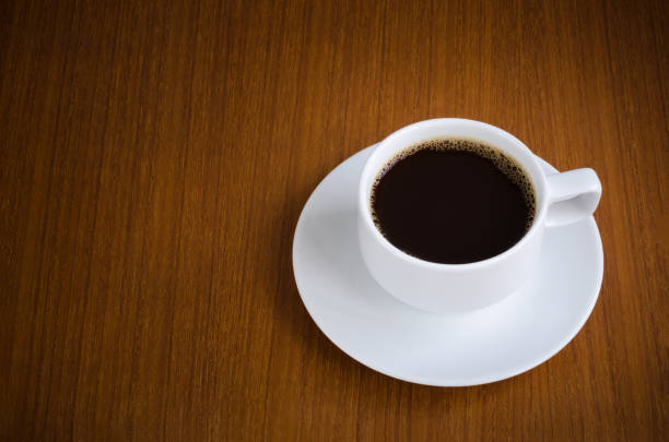 istock Black coffee in white ceramic cup on saucer over dark teak wood background with copy space 812936684
