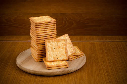 Fresh baked cream crackers in stacks over wooden cutting circle board on wood table and dark brown background with copy space for text decoration
