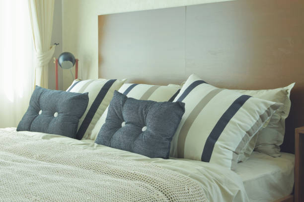 istock Gray and brown strip pillows setting on white linen bedding with brown wooden headboard 812942580