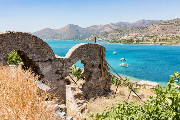 Ruins on top of Spinalonga. Picturesque view to the blue sea with boats and island with mountain. Lasithi, Greece.