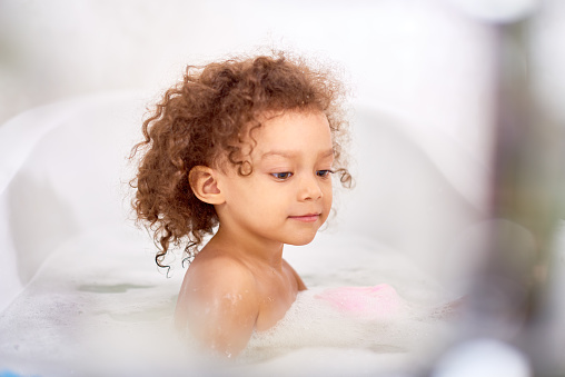 Portrait of cute semi African boy taking bubble bath in white bathroom