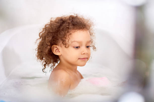 Cute Curly Child Enjoying Bubble Bath Portrait of cute semi African boy taking bubble bath in white bathroom girls bath stock pictures, royalty-free photos & images