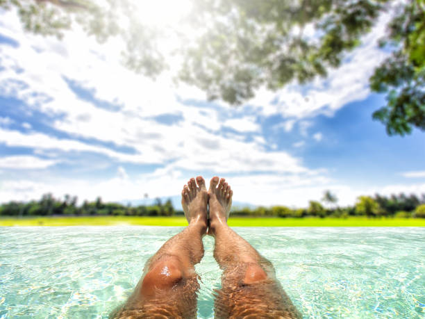 istock Legs of man relaxing in pool with countryside view 812983652