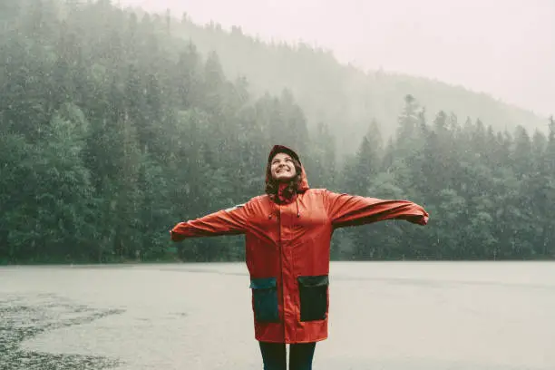 Photo of Woman in raincoat standing near the lake under the pouring rain
