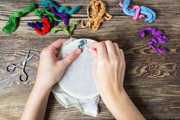 female hand embroidered cross on the canvas. wooden table and thread stranded cotton. - textile sewing women part of imagens e fotografias de stock