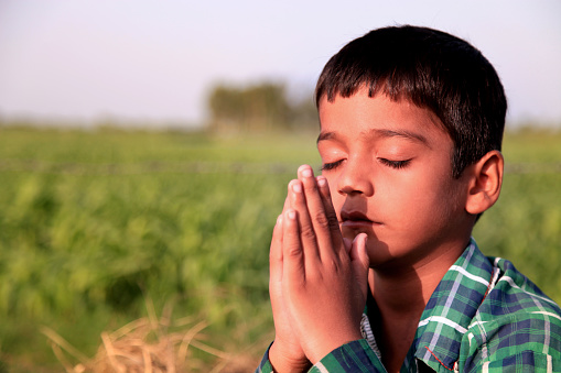 Elementary age schoolchild praying to god outdoor in the nature.