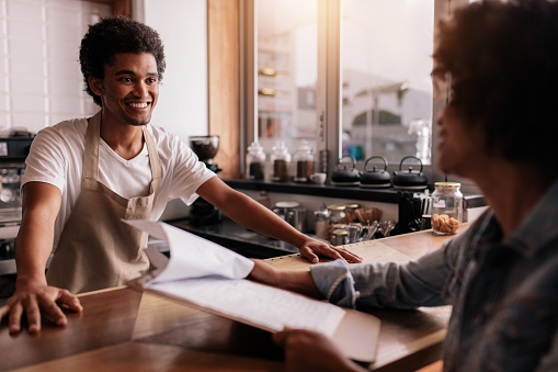 Young male barista taking an order from a female customer in a coffee shop and smiling