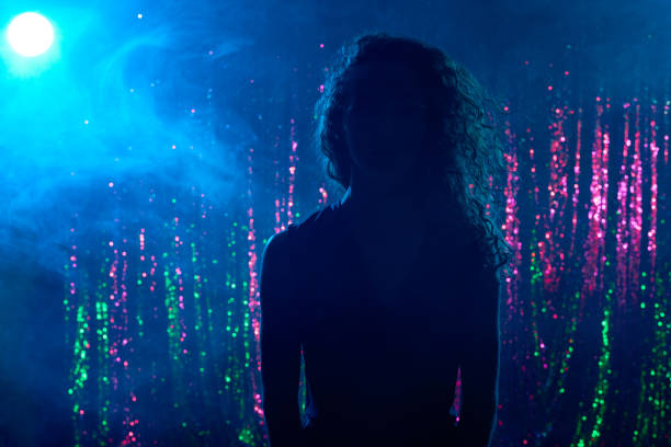 Portrait of young woman standing on stage in night club in dim blue lighting
