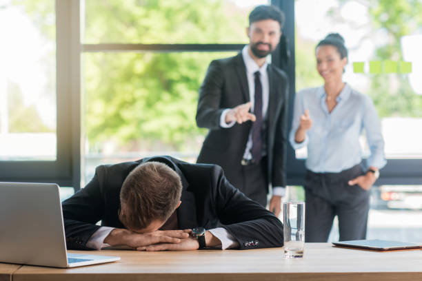 istock tired businessman at sitting workplace with laptop in office while colleagues standing behind 813008916