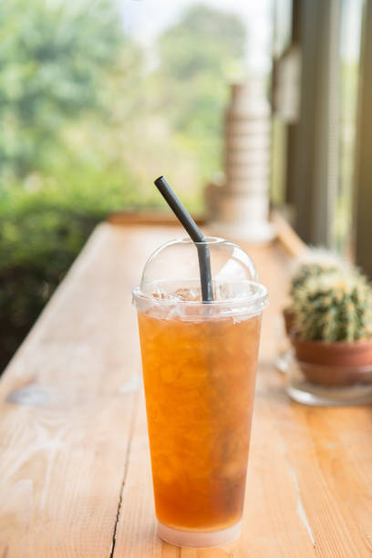 Iced lemon tea with soda in a tall plastic cup on the wooden table. In homemade coffee shop.